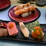 Assortment of sushi and sashimi on a black plate.