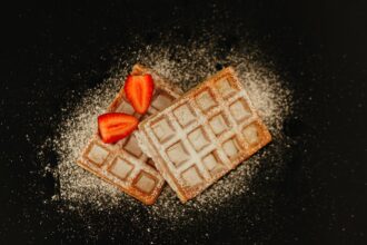 Tasty Belgian waffles topped with fresh strawberries and sugar dusting.