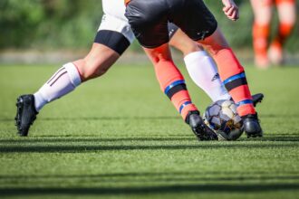 woman in black and white soccer jersey kicking soccer ball on green field during daytime