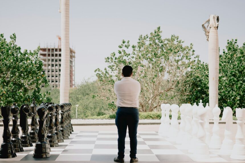 Man standing between giant chess pieces on a board